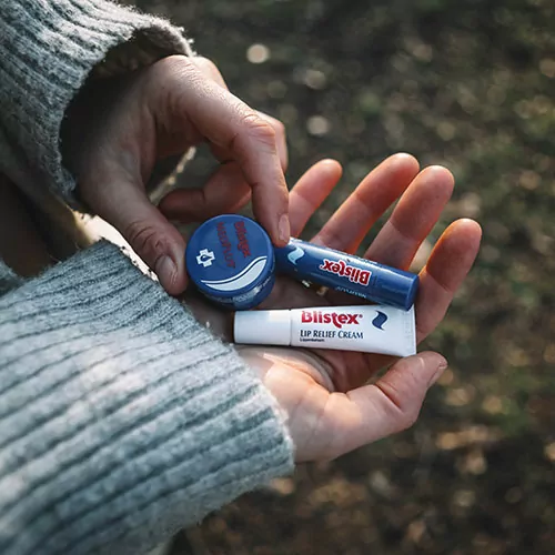 Mehrere Blistex-Produkte liegen in den Handinnenflächen einer Person in der Natur.